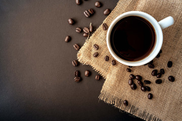 Wall Mural - A cup of coffee and coffee bean grain on sack fabric put on black wood table background include copyspace for add text or graphic