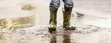 Child With Rain Boots Jumps Into A Puddle