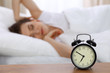 © rogerphoto - Beautiful sleeping woman resting in bed and trying to wake up with alarm clock