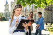 © A Stock Studio - Young female student holds electronic digital tablet standing in the background of a group of students on the university campus. Student life.