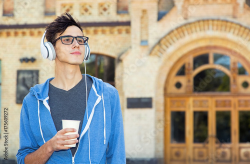Plakat Młody człowiek w słuchawkach słucha muzyki i pije kawę.