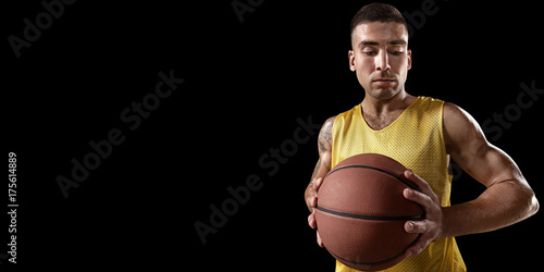 Zdjęcie XXL Gracz koszykówki trzymać piłkę do koszykówki. Odosobniony gracz koszykówki na czarnym tle. Gracz nosi ubrania niemarkowe.