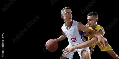 Zdjęcie XXL Dwóch graczy w koszykówkę walczy o piłkę do koszykówki. Odosobneni gracze koszykówki na czarnym tle. Gracz nosi ubrania niemarkowe.