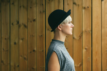 Side View Of A Blonde Woman In Front Of A Wooden Wall.