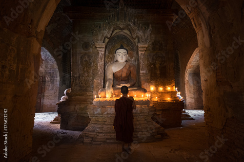 Fotomural Young novice monk praying with candles in front of buddha statue inside old pago