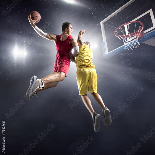 Zdjęcie XXL Gracz koszykówki robi slam dunk na dużej profesjonalnej arenie. Gracz leci w powietrzu z piłką. Przeciwnicy próbują zapobiec uderzeniu piłki w pierścień do koszykówki.