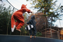 Cute Girl In Fox And Boy In Raccoon Costume Jumping On Trampoline