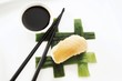 Sushi Nigiri, made with salmon and rice, placed beside black chopsticks and a bowl of soy sauce on interwoven leek strips