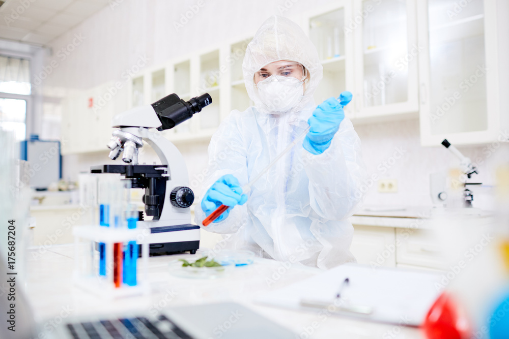 Concentrated female researcher wearing hazmat suit filling test tube ...