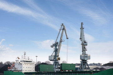 Shot of two old, rusty, grey port cranes with big hooks, lifting cargo in ship on clear blue sky background. Equipment for unloading ships and barges. Preparing for export world wide. Work at harbor