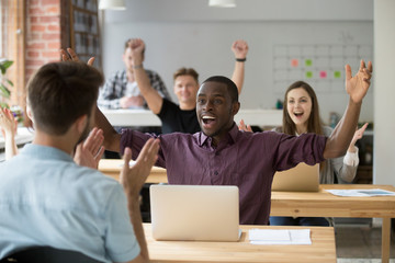 Sticker - Young african american office worker throws hands in air celebrating achievement at work. Coworkers around cheering and clapping hands. Rewarding outcome, received promotion, achieved success concept.