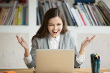 Young Businesswoman Looks At Laptop Screen With Expression Of Joy And Excitement. Surprised Female Office Worker At Workplace Looking At Computer With Big Smile. Business Woman Received Promotion.