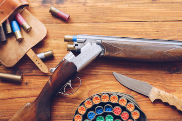 Hunting equipment. Shotgun, hunting cartridges and hunting knife on wooden table.