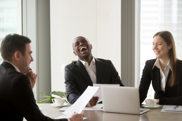 Wall Mural - African american man laughing during successful negotiations with caucasian partners. Job applicant made pleasant first impression on recruiters with joke at interview. Good relationship in office