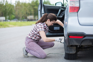 Wall Mural - A beautiful young woman repairing a car, unscrew the wheel