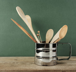 Wall Mural - wooden kitchenware in metal jug  on old wooden table over green background