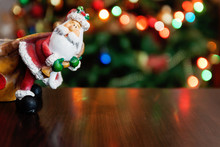 Santa Claus Toy Brings Christmas Tree At Blue Snowy Night Bokeh  Background And Blurred Lights Foreground. Red Lantern Torch To Light The Way. Big Copyspace Concept New Year`s Market Banner, Poster.
