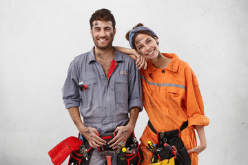 Wall Mural - Smiling dirty woman leans on shoulder of man mechanic, helps him to repair car on work station, rejoice their succeess, earned much money, work as friendly team. Repairing and renovation concept