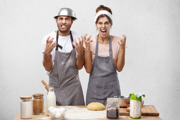 Irritated female and male cooks, keep hands in furious gesture, being annoyed with chef who asks to cook many dishes for tomorrow. Nervous housewife and husband screams in panic. Negative emotions