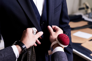 closeup of tailor fitting bespoke suit to model, hands with tape measure and pin cushion fixing jack