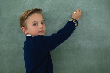 Schoolboy writing with chalk on chalkboard