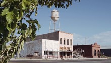 Abandoned Ghost Town With Water Tower. Shot Moves From A Tree And Reveals An Abandoned Ghost Town Main Road With A Water Tower
