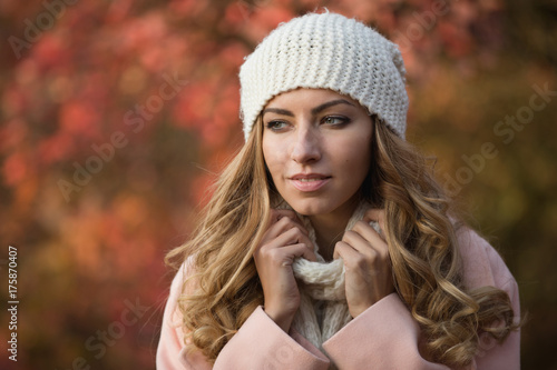 Plakat Ładny kobieta portret w białym kapeluszu przy jesień dniem, ona stoi w parku, kolorowy ulistnienie wokoło