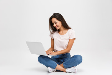 Wall Mural - Photo of young smiling woman with long hair, holding and using laptop, while sitting with crossed legs