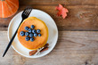Pumpkin pancakes with blueberries and honey on white plate over old wooden table. Table top view, copy space for text