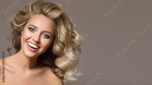 Obraz na płótnie Blondynki kobieta z kędzierzawy piękny włosy ono uśmiecha się na popielatym tle.