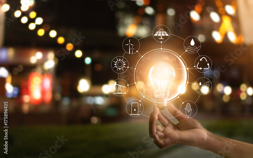 Fotografía Hand holding light bulb in front of global, show the world's consumption with icons energy sources for renewable, Ecology concept