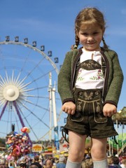 Mädchen in Lederhose vor Riesenrad auf Rummelplatz