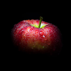 Water droplet on glossy surface of red apple on black background