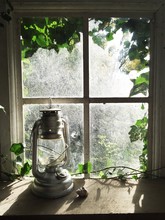 Hurricane Lantern In Front Of An Ivy-framed Window.