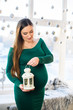 © Nestyda - Beautiful pregnant girl with Big belly near the window on a Christmas, having a rest on Christmas holidays before the new year. the concept of a new life