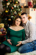 © Nestyda - Beautiful pregnant couple in love on the background of a Christmas tree, having a rest on Christmas holidays before the new year. Big pregnant belly