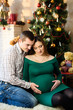 © Nestyda - Beautiful pregnant couple in love on the background of a Christmas tree, having a rest on Christmas holidays before the new year. Big pregnant belly