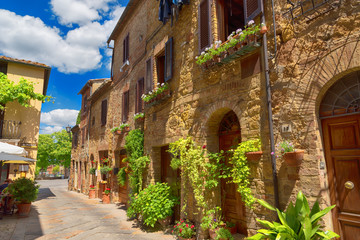 Wall Mural - Beautiful narrow street with sunlight and flowers in the small magical and old village of Pienza, Val D'Orcia Tuscany, Italy.