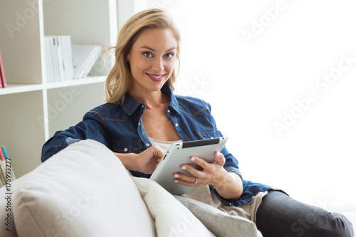 Plakat Piękna młoda kobieta używa jej cyfrową pastylkę w domu.