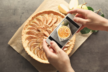 Woman taking photo of tasty pear tart with mobile phone in kitchen