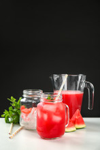 Jug And Mason Jars With Watermelon Juice On Table Against Black Background