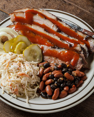 A plate of sliced brisket  with baked beans, cole slaw and dill pickles