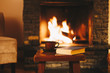Cup of hot tea with a book in front of warm fireplace