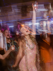 Happy New Year party in blurred motion. Joyful lady at Christmas discotheque, modern youth life, active company with drinks in night club