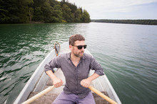 A Man Is Rowing A Rowboat On A Lake.