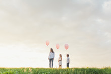 Mother And Her Kids Holding Pink Balloons Against A Big Cloudy Sky