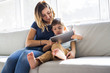 © Louis-Paul Photo - Little boy with digital tablet sitting on sofa, on home interior background with mom