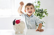 © Louis-Paul Photo - childhood, money, investment and happy people concept - smiling little boy with piggy bank and money at home
