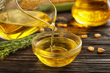 Wall Mural - Pouring corn oil from pitcher into glass bowl on wooden background