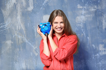 Sticker - Beautiful young woman with piggy bank on grunge background